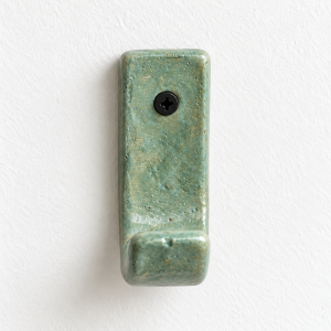 Sage green ceramic wall hook mounted on a white wall with a black screw