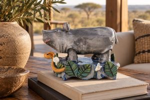 Grey ceramic hippo sculpture on a decorated base displayed on books in a warm room setting