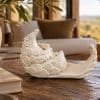 White ceramic pangolin reclining on its back, displayed on a wooden table in a warm room setting